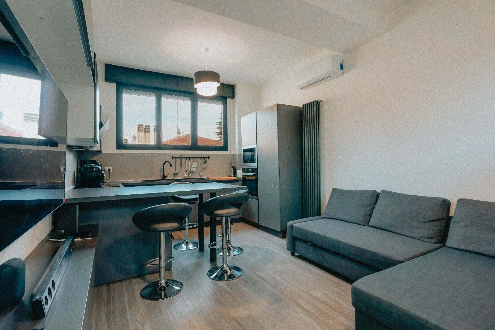 The finished Bologna micro-home: open-plan kitchen and living room with bar stools and a grey corner sofa
