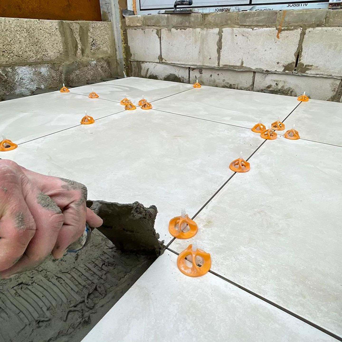 Large floor tiles being set with orange tile levelling spacers